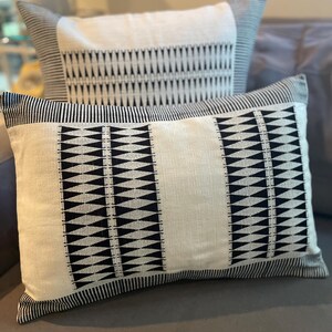 Op de afbeelding: Twee decoratieve kussens met een zwart-wit geometrisch patroon. De kussens zijn gemaakt van een zachte, witte stof met zwarte driehoekige ontwerpen.