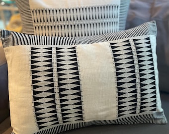 Puede incluir: Dos almohadas decorativas con un patrón geométrico en blanco y negro. Las almohadas están hechas de una tela blanca suave con diseños triangulares negros.