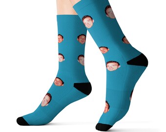 Op de afbeelding: Een paar blauwe sokken met een herhalend patroon van een mannengezicht.