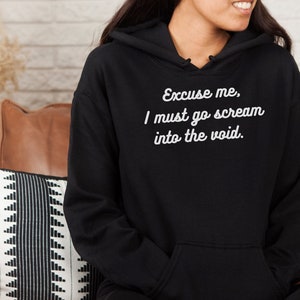 May include: Black hooded sweatshirt with white text that reads "Excuse me, I must go scream into the void."