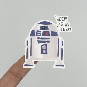 May include: A sticker featuring a stylized illustration of the Star Wars droid R2-D2. The droid is primarily white and blue with red and black accents. Text bubbles above the droid read "BEEP! BOOP! BEEP!"