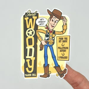 May include: A Sheriff Woody sticker featuring the character in a cowboy hat, vest, and boots. The sticker includes text that says "Hey Howdy Hey!" and "From the Hit Show!" and "Talking Doll".
