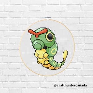 May include: A green and yellow pixel art cross-stitch pattern of a Pokemon character, Caterpie, on a white background. The character is in a curled up position with its red eyes visible.