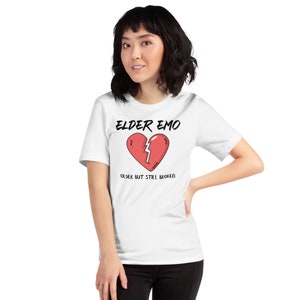 May include: White t-shirt with a black graphic of a broken heart with stitches and the text "Elder Emo" and "Older but still broken".