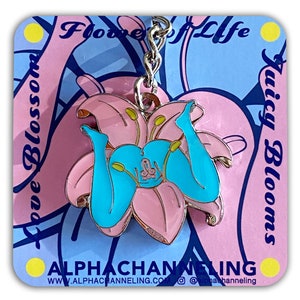 May include: A pink and blue enamel keychain featuring a stylized flower design with a pair of turquoise legs. The keychain hangs from a silver chain and is set against a card with text that reads "Flowers of Life" and "Juicy Blooms". The card also has the website address.