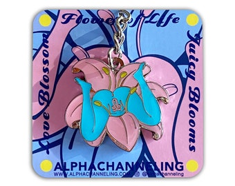May include: A pink and blue enamel keychain featuring a stylized flower design with a pair of turquoise legs. The keychain hangs from a silver chain and is set against a card with text that reads "Flowers of Life" and "Juicy Blooms". The card also has the website address.