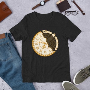 May include: A black t-shirt with a graphic of a clock face with a bite taken out of it. The graphic is in gold and white and says "Time & Seasons".