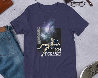 May include: A navy blue t-shirt with a graphic of an astronaut floating in space with a galaxy background. The text "THE HEAVENS DECLARE THE GLORY OF GOD THE SKES PROCLAIM THE WORK OF HIS HANDS 19:1 PSALIMS" is printed on the shirt.