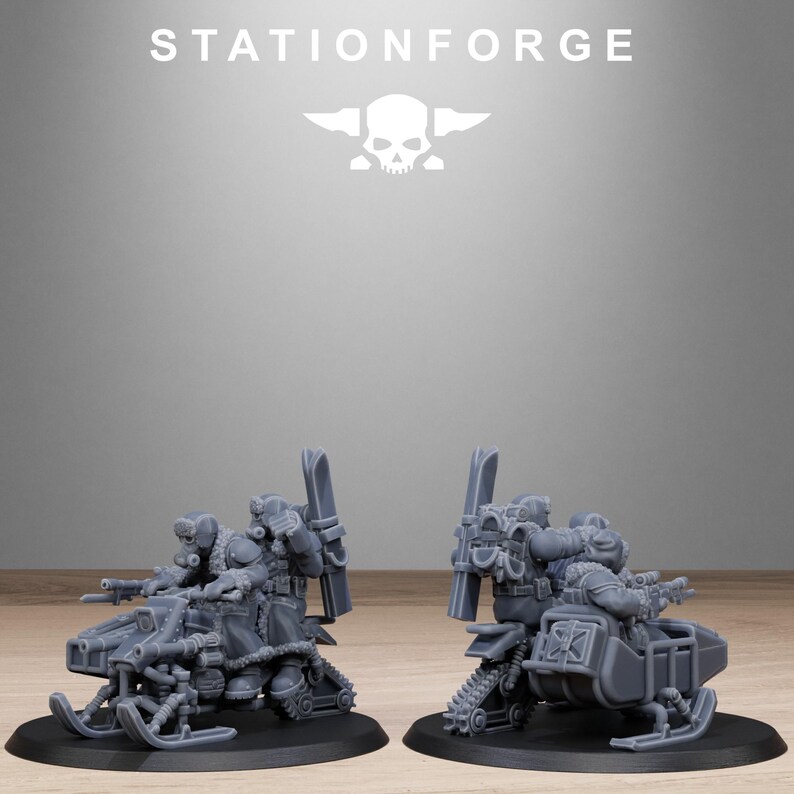 May include: Two gray miniature models of snowmobiles with detailed weaponry and figures. The models are on black bases, with the text "STATIONFORGE" and a skull logo above them. The snowmobiles have skis and tracks.