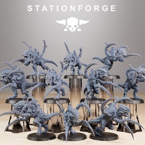 May include: A set of 12 grey plastic miniature figures of alien creatures with multiple legs and claws. The figures are posed in various action stances. The figures are arranged on a wooden surface with grey plastic bases.
