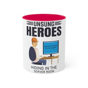 Può includere: Una tazza in ceramica bianca con un bordo rosso. La tazza presenta un'illustrazione di un cartone animato di una persona seduta davanti a un computer con il testo "DESTROY THE UNIVERSE? YES NO NOT TODAY" sullo schermo. Il testo "UNSUNG HEROES HIDING IN THE SERVER ROOM" è stampato sulla tazza.