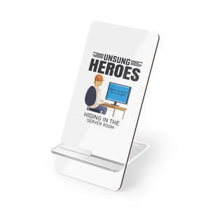 Può includere: Supporto per telefono bianco con un'illustrazione di un cartone animato di una persona che lavora al computer. Il testo sul supporto recita "Unsung Heroes Hiding in the Server Room".
