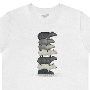 Könnte beinhalten: Weißes T-Shirt mit einem Grafikdruck von einem Stapel Capybaras, mit einem schwarzen Capybara oben, stehend auf einem kleinen Felsen im Wasser.