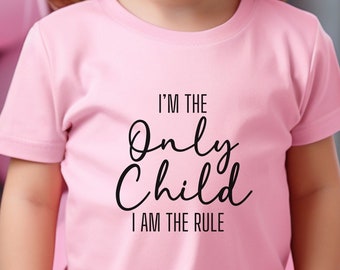 Op de afbeelding: Een roze T-shirt met de tekst "I'm the Only Child I am the Rule" in zwarte letters.