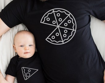 May include: A father and child wearing matching black t-shirts with a white outline of a pizza slice. The father's shirt has a whole pizza with a slice missing. The child's shirt has a single slice of pizza.
