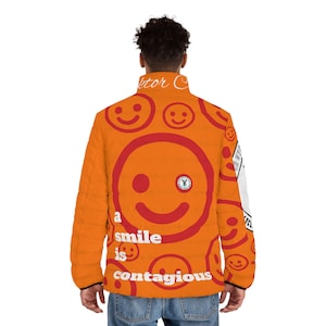 May include: Orange puffer jacket with a repeating pattern of red smiley faces. The jacket has a white zipper and a white collar. The text "a smile is contagious" is printed on the jacket.