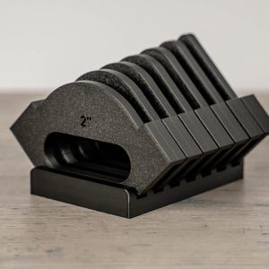 May include: A set of black, wedge-shaped objects, each approximately 2 inches in width, arranged in a holder. The objects have a textured surface and are designed to stand upright. The holder is also black and has a rectangular base.