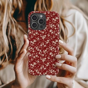 May include: A red phone case with a white floral pattern. The case has a cutout for the camera lens.