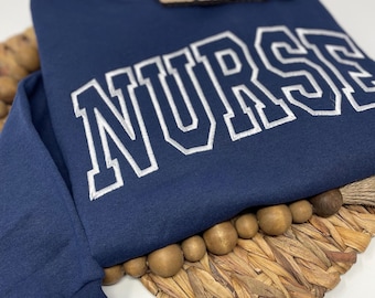May include: Navy blue sweatshirt with the word "NURSE" embroidered in white on the front.