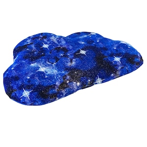 May include: Cloud-shaped pillow with a celestial design. The pillow features a dark blue background with white stars and nebulas. The pillow is made of soft fabric and is designed to resemble a cloud.