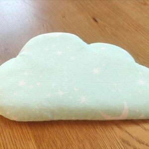 May include: A cloud-shaped pillow in a soft, mint green color. The pillow is decorated with a pattern of white stars and crescent moons. The pillow is made of a soft fabric and is designed for comfort and decoration.