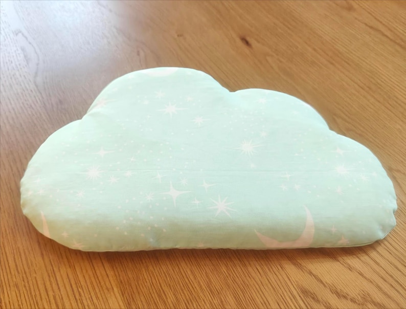 May include: A cloud-shaped pillow in a soft, mint green color. The pillow is decorated with a pattern of white stars and crescent moons. The pillow is made of a soft fabric and is designed for comfort and decoration.