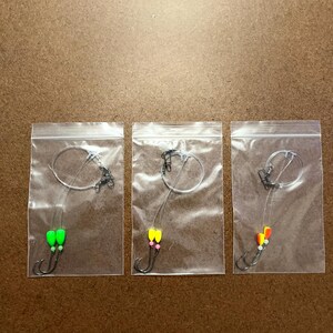 May include: Three clear plastic bags each containing a fishing lure with a single hook and two beads. The beads are green and white, yellow and pink, and orange and white.