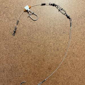 May include: A fishing rig with a swivel, beads, and a hook. The rig is made of clear fishing line and has a white plastic bead.