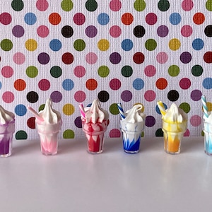 May include: Six miniature milkshakes with white whipped cream and colorful swirls. Each milkshake has a striped straw.