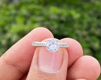 May include: A silver ring with a large, clear, round gemstone surrounded by smaller gemstones. The ring is set on a plain band.