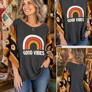 May include: A charcoal gray top with a wide scoop neckline and loose, flowing sleeves featuring a patchwork pattern in shades of mustard yellow, black, and cream. The front displays a graphic of a rainbow with the text GOOD VIBES below it.