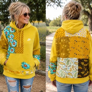 May include: A mustard yellow hooded sweatshirt featuring a Nike logo on the chest and a patchwork design with various floral, paisley, and geometric patterns in shades of teal, white, and brown on the front and back, including a front kangaroo pocket.