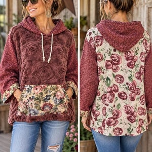 May include: A long-sleeve hooded sweatshirt featuring a textured maroon faux-fur body, a floral print kangaroo pocket, and floral print sleeves. The back displays a cream-colored fabric with a maroon rose pattern and a matching maroon hood.