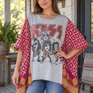 May include: A grey short-sleeve top featuring a distressed KISS band graphic on the front. The garment has wide, loose-fitting sleeves and side panels in a vibrant magenta and gold geometric pattern with visible stitched detailing.