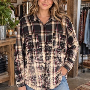 May include: A long-sleeve button-down shirt featuring a black, tan, and maroon plaid pattern with a bleached, distressed effect across the lower half and two chest pockets. The shirt is paired with blue denim jeans.
