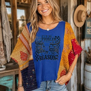 May include: A blue short-sleeve top featuring a central graphic of a bull skull, flowers, and a checkerboard pattern with the text IF I'M THE PROBLEM THEN YOU MIGHT BE THE REASON. The sleeves are made of multicolored patchwork fabric with floral prints.