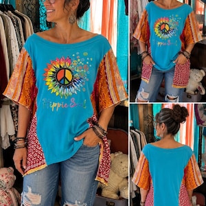 May include: A turquoise short-sleeve top featuring a central graphic of a rainbow-colored sunflower with a peace sign in the middle and the text Hippie Soul. The garment has contrasting side panels in red floral and orange patterned fabric.