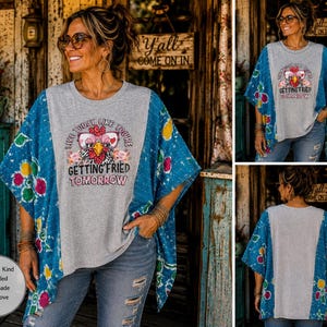 May include: A grey t-shirt with a blue patterned poncho-style overlay. The shirt features a graphic of a chicken wearing glasses with the text: Live today like you're getting fried tomorrow. The blue overlay has a floral and speckled pattern.