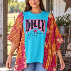 May include: A turquoise t-shirt featuring the text DOLLY in black letters over a pink star and the word Parton in black script. The shirt has loose, short sleeves made of orange and pink patterned fabric with a floral design.