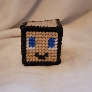 May include: A small, brown, pixelated figure with a black outline. The figure has blue eyes, a white smile, and a black nose.