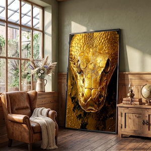 Könnte beinhalten: Ein großes, rechteckiges Wandbild mit einer detaillierten Nahaufnahme eines goldenen Schlangenkopfes mit markanten Schuppen und dunklen, mandelförmigen Augen. Das Kunstwerk ist in einem dünnen schwarzen Rahmen gefasst und zeigt eine metallisch reflektierende Textur.