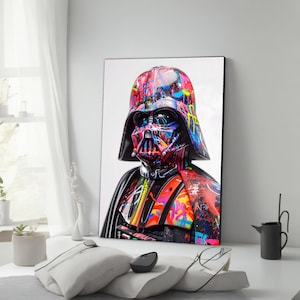 May include: A framed art print of Darth Vader, featuring a vibrant graffiti-style design. The artwork showcases a colorful explosion of paint splatters across Vader's helmet and armor, with shades of red, blue, yellow, and green. The portrait is set against a white background.