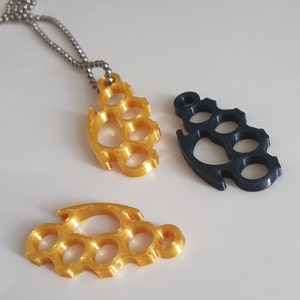 May include: Three metal keychains in the shape of a knuckle duster. One is gold, one is black, and one is silver. The gold and black keychains are hanging from a silver chain.
