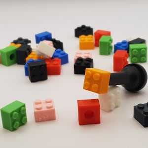 Könnte beinhalten: Eine Sammlung bunter Plastikbausteine in verschiedenen Formen und Größen, darunter ein schwarzer Gummistopfen für Flaschen.