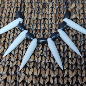 May include: A black and white necklace with white pointed spikes and black beads.