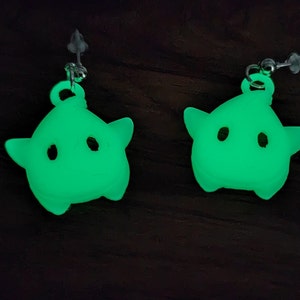 May include: A pair of green glow-in-the-dark star-shaped earrings. The earrings are made of a soft, flexible material and have a cute, cartoonish design.