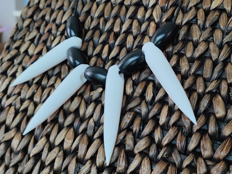 May include: A black and white necklace with sharp, pointed teeth-like pendants. The necklace is made of plastic and has a black cord.
