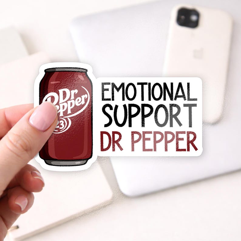 May include: A sticker featuring a Dr Pepper can and the text "EMOTIONAL SUPPORT DR PEPPER." The Dr Pepper can is a dark red color with white text. The text is in black and red.