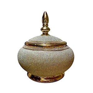 Könnte beinhalten: Ein dekoratives Gefäß mit Deckel und gold-silbernem Glitzer-Finish. Das Gefäß hat einen abgerundeten Körper und einen goldenen Sockel und Zierleisten. Der Deckel ist mit einer goldenen Spitze versehen. Das Gefäß ist für dekorative Zwecke bestimmt.
