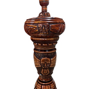 May include: A tall, intricately carved wooden lamp base with a dark brown finish. The base features a stylized human face and geometric patterns.
